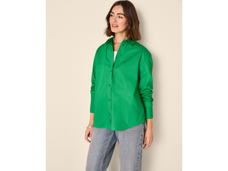 Woman in a green button-up shirt and blue jeans, looking to the side.