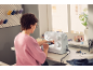Woman sewing with a sewing machine, with sewing supplies and thread spools on the table.