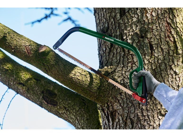 Green bow saw cutting a tree branch, held by a gloved hand.