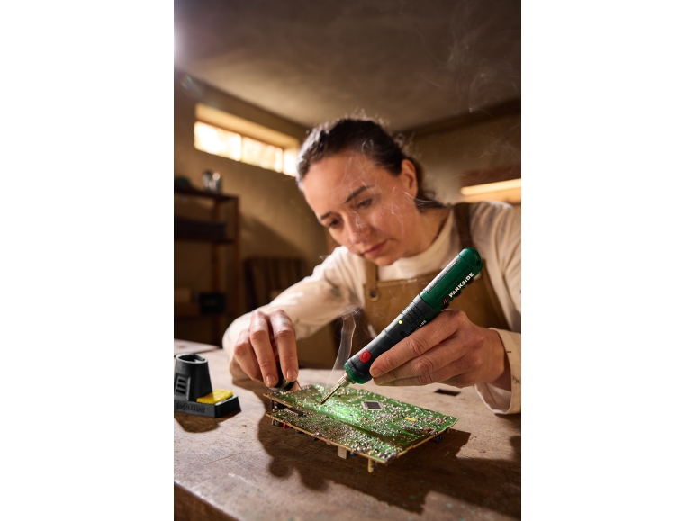 Woman soldering a circuit board with a soldering iron and solder wire.