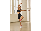 Woman in black ribbed sports bra and cycling shorts, white and pink trainers, dancing.