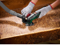 Person in gloves sanding a wooden surface with a delta sander and dust extraction attachment.
