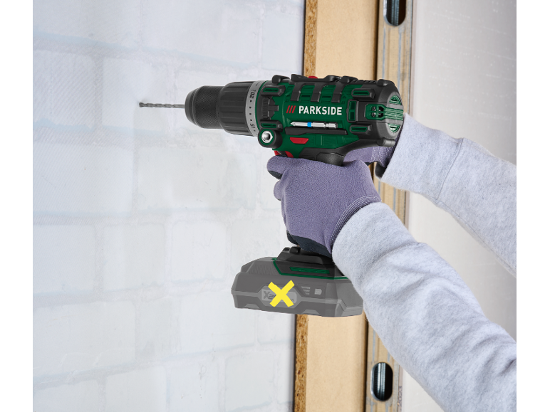 Gloved person drilling into a white brick wall with a cordless drill.