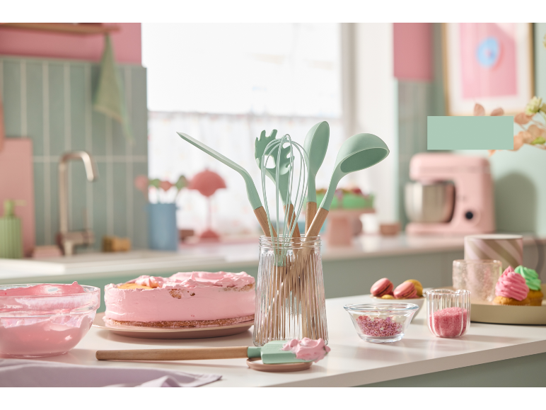 Kitchen utensils and a pink cake in a pastel-themed kitchen.