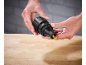 Hands holding a black drill chuck with a golden drill bit over a wooden surface.