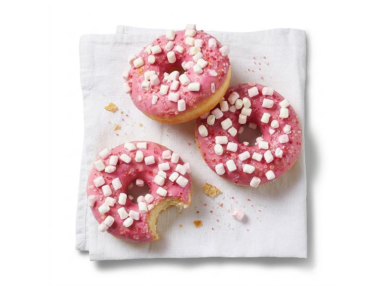 Three pink glazed donuts with marshmallows and sugar sprinkles on a white towel.
