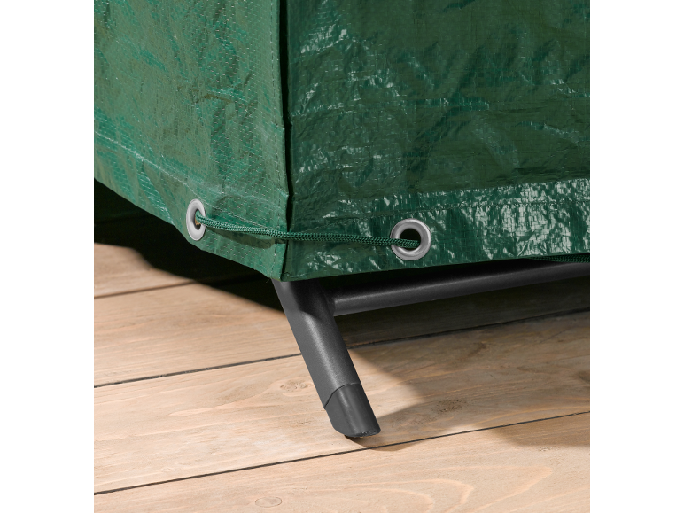 Green tarpaulin cover with eyelets and drawstring, covering furniture on a wooden floor.
