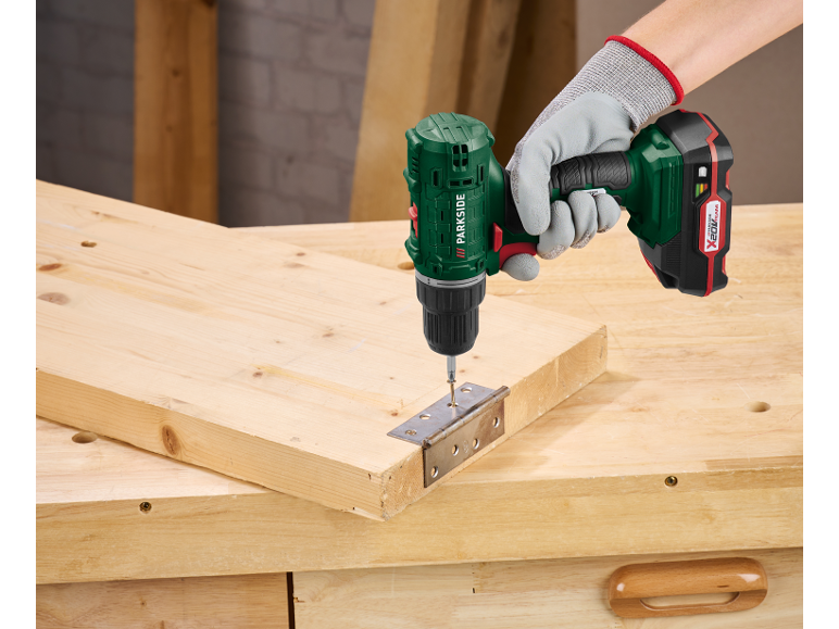 A cordless drill is used to attach a hinge to a wooden board.