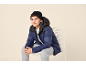 Boy in black beanie and blue puffer jacket sitting on a chair.