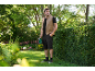 Man in a vest and shorts holding a hedge trimmer in a garden.