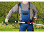 Man in work overalls using a cordless pole hedge trimmer with a shoulder strap.