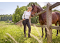 Woman in black trousers and white top petting a brown horse by a wooden fence.