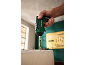 Hand holding a green cordless screwdriver with a bit, ready to screw into wood.