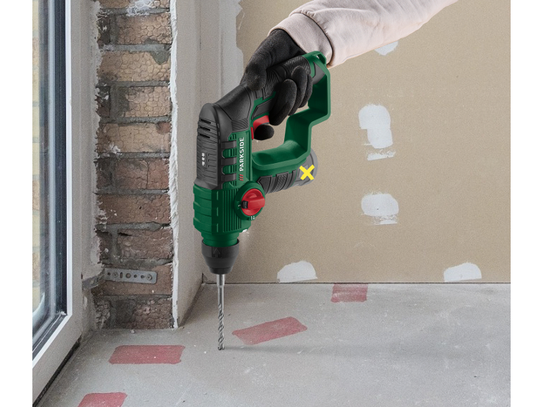 Green hammer drill drilling into a concrete floor on a construction site.