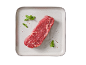Raw cut of beef with herbs and spices on a light-colored plate.