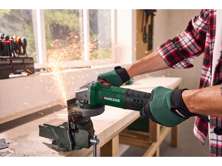 Man in gloves cuts metal with an angle grinder, sparks flying in a workshop.