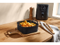 Black silicone basket with chicken nuggets, onion rings, and fries, next to an air fryer.