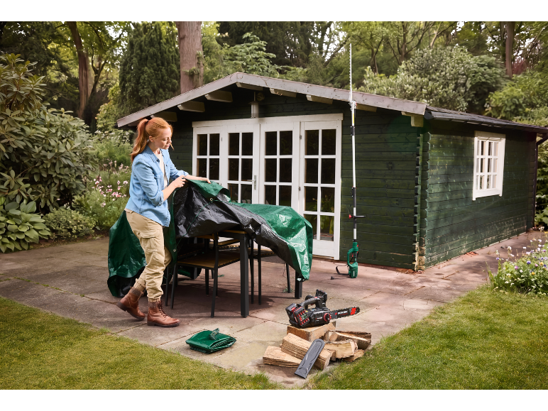 Woman covering garden furniture with a tarp, with a chainsaw and firewood nearby.