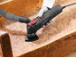 Multi-tool with vacuum attachment sanding a wooden surface.