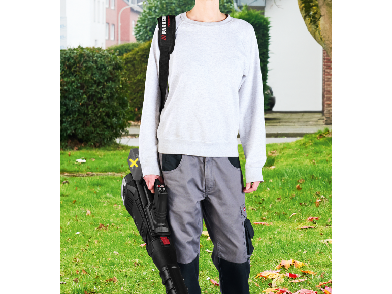 Person holding a leaf blower, wearing work trousers and a sweatshirt, with a shoulder strap.