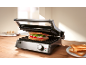 Sandwich in an open panini grill on a wooden table.