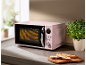 Pink microwave on a kitchen counter with herbs and bread slices.