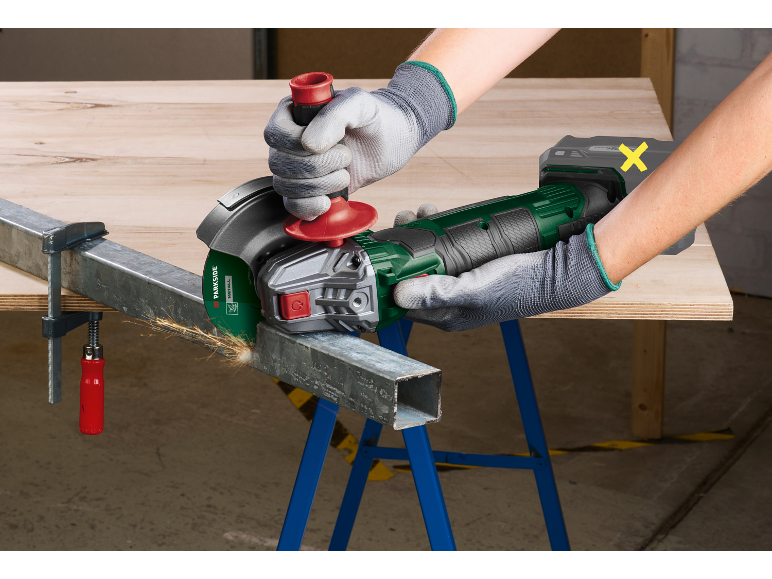 Angle grinder cutting a metal profile clamped with a G-clamp on a workbench.