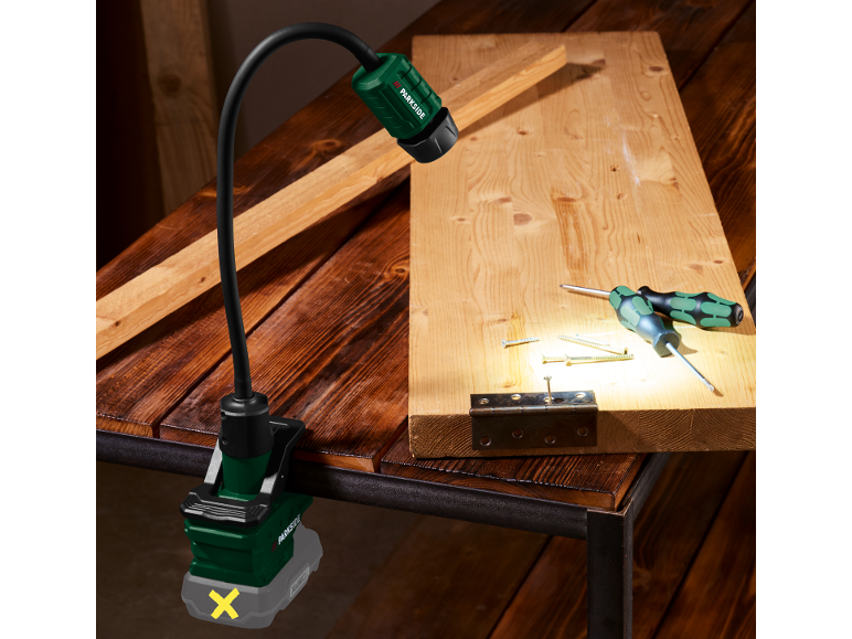 Work light with clamp illuminates a wooden board with tools and screws.