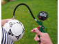 Digital tire pressure gauge with hose inflating a soccer ball on a lawn.
