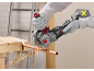 Man cutting a copper pipe with a cordless angle grinder, generating sparks.