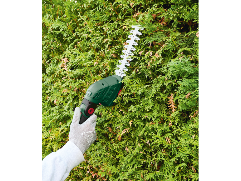 Electric hedge trimmer cutting a green hedge with a gloved hand.