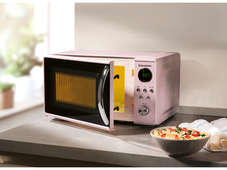 Pink microwave with an open door and a bowl of pasta on the kitchen counter.