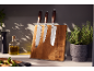 Wooden knife block with three knives, olive oil, pepper mill, and herb plant in a kitchen.