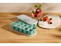 Two ice cube trays, one filled with ice, next to a berry drink and fresh fruit.