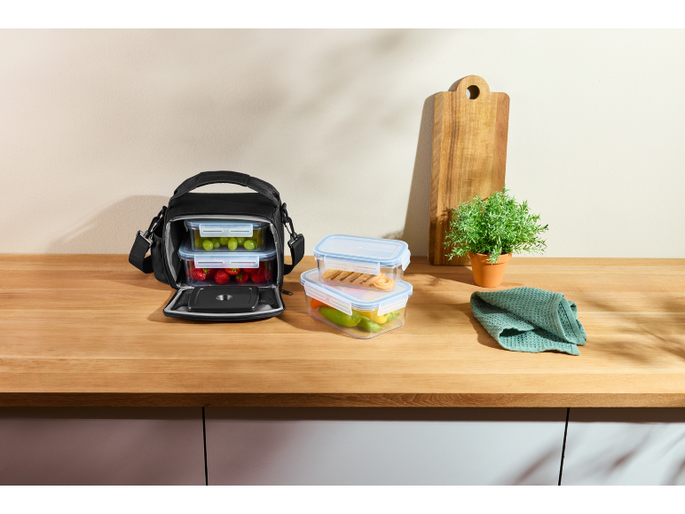 Picnic bag with food containers filled with fruit and vegetables on a wooden counter.