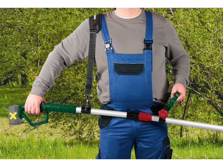 Man in work overalls using a cordless pole hedge trimmer with a shoulder strap.