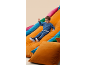 Boy in blue tracksuit sliding down an orange cushion, surrounded by colorful cushions.