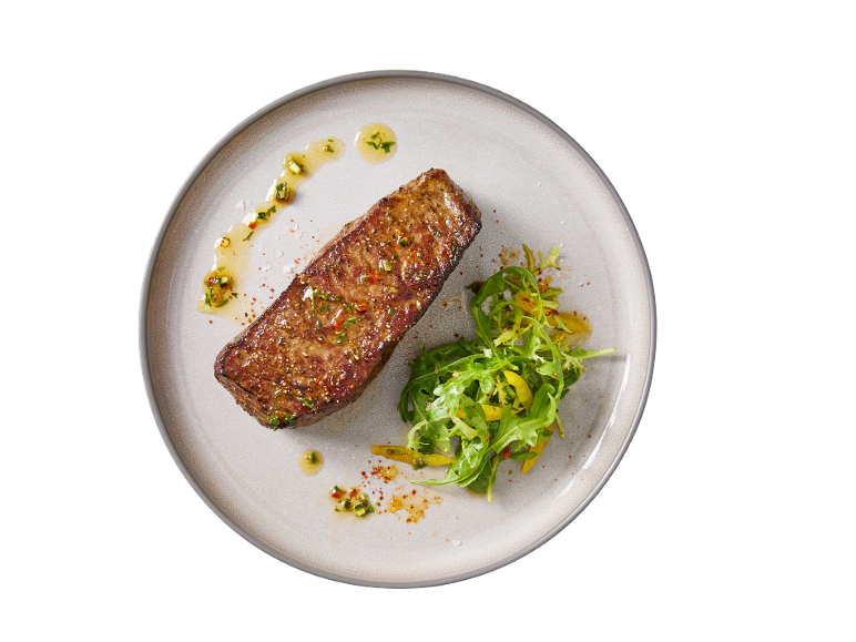 Grilled steak with salad and spicy dressing on a plate.