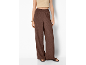 Woman in brown wide-leg trousers and a beige crop top, with sandals and a gold bracelet.