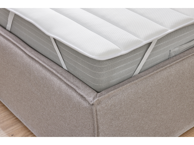 Close-up of a mattress topper with elastic straps on a bed base.
