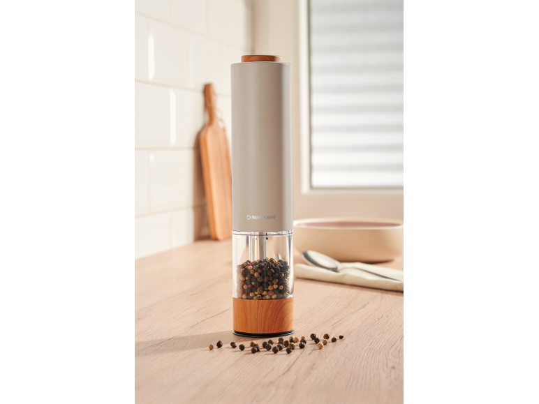 Electric salt and pepper grinders with wooden base and peppercorns in the kitchen.