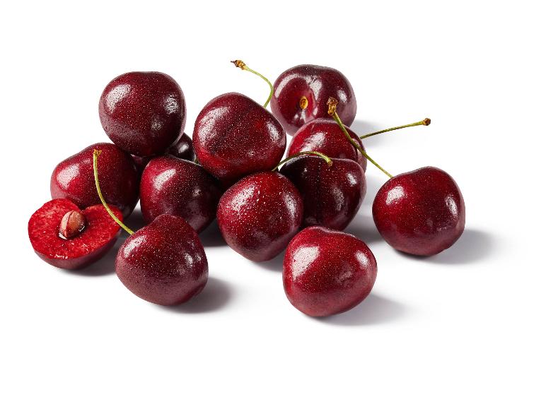 Pile of fresh, dark red cherries with water droplets, one cut in half revealing the pit.