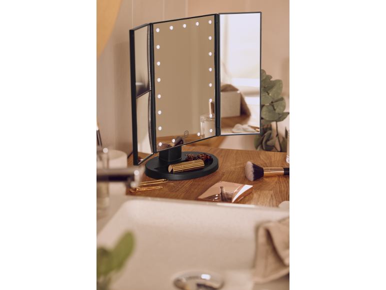Lighted cosmetic mirror on a wooden bathroom shelf with makeup.