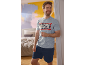 Man in grey and dark blue short pajamas with superhero print, smiling in the bedroom.