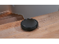 Black robotic vacuum cleaner on a wooden floor next to stairs.