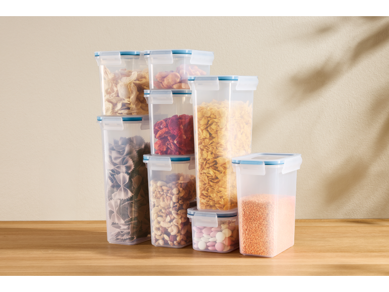 Clear storage containers with pasta, cereal, dried fruit, and nuts on a wooden table.