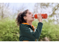 Young woman drinking from an orange water bottle, wearing a green jacket with an orange hoodie.