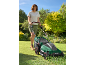 Woman mowing a lawn with a green electric lawnmower on a sunny day.