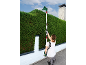 Woman trimming a tall hedge with a long-reach hedge trimmer.