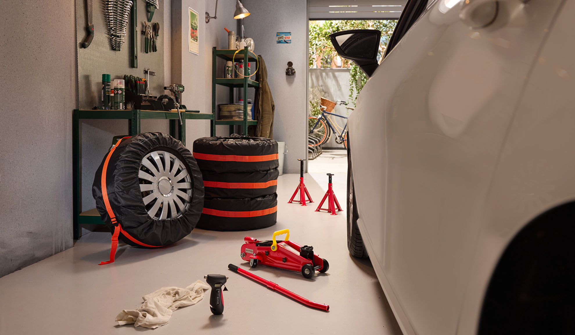 Car tires with covers, a jack, and tools in a garage.
